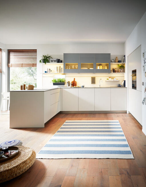 Klare Linien zeichnen diese grifflose Küche in mattem Weiß aus. Pflanzen und offene Regale machen sie wohnlich und verleihen ihr eine persönliche Note.